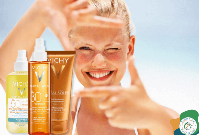 Ragazza in costume in spiaggia che incornicia il viso con le mani a forma di fotocamera, accanto a solari Vichy, simbolo di protezione e bellezza sotto il sole.