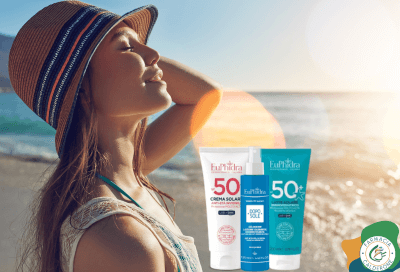 Ragazza in spiaggia di fronte alla riva, con il viso rivolto verso il sole e i solari Euphidra accanto, simbolo di protezione e benessere sotto il sole estivo.