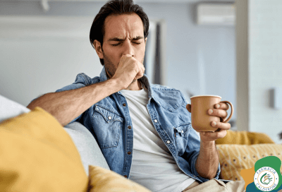 Uomo seduto sul divano con una tazza in mano mentre tossisce.