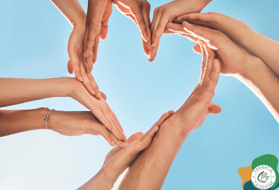 Mani di più persone che formano un cuore contro il cielo azzurro, simbolo di prevenzione e unione per la salute del cuore.