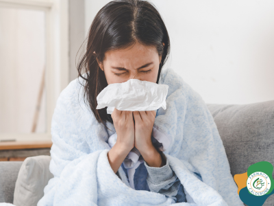 Donna con una coperta che si soffia il naso con un fazzoletto, sintomo tipico dell’influenza stagionale.